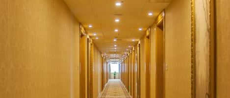 A long, narrow hallway with a patterned carpet, doors on both sides, and recessed lighting on the ceiling.
