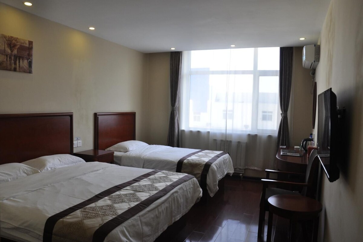 Ein Hotelzimmer mit zwei Betten, einem Schreibtisch, einem Stuhl, einem Fernseher und einem Fenster mit Vorhängen.
