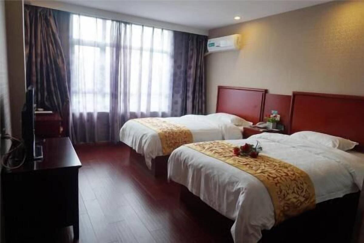 A hotel room with two beds, a desk, and an air conditioning unit.