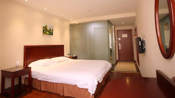 A hotel room with a bed, bedside table, a mirror, and a door leading to a bathroom. - Greentree Inn Express (Nanjing)