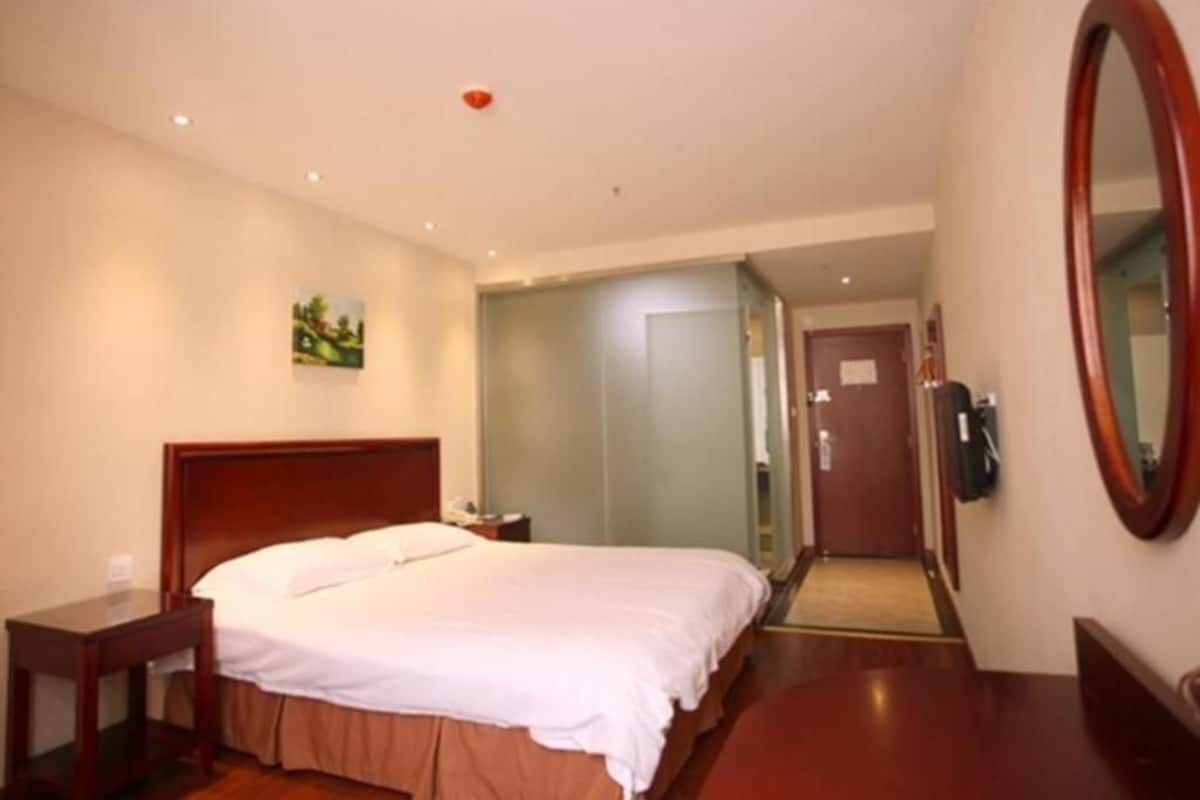 Hotellihuone, jossa on sänky, yöpöytä ja peili.