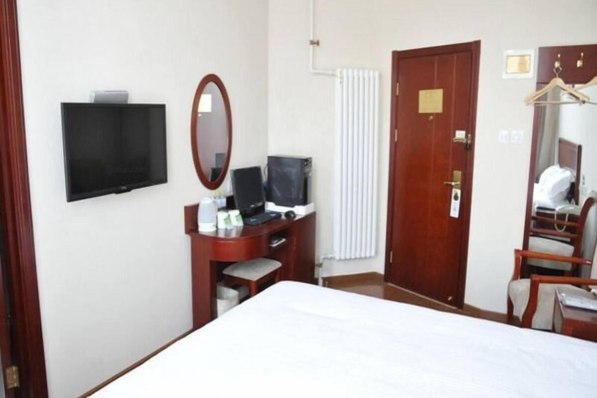 Habitació d'hotel amb un llit, un escriptori amb un ordinador, una televisió, un mirall i un armari.