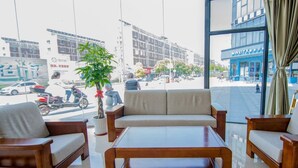 A modern hotel lobby with a sofa, chairs, a coffee table, and a large window offering a view of the street. - Greentree (Nantong)
