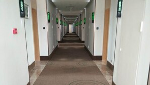 A long, narrow hotel corridor with a patterned carpet, doors on both sides, and green directional signs. - Greentree (Nantong)