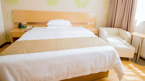 A hotel room with a large bed, a bedside table with a phone, a chair, and a small round table. - Greentree (Nantong)