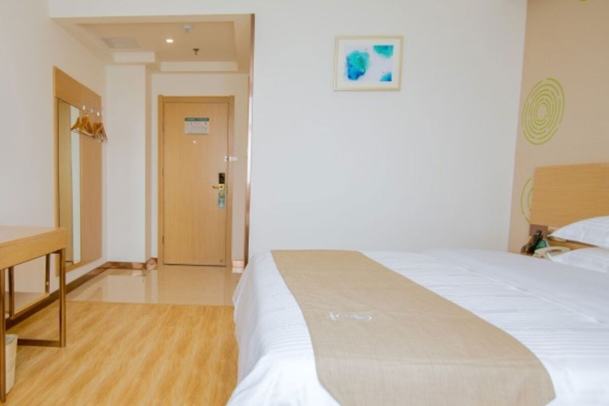 A hotel room with a bed, a wooden bench, a door, and a wall with a framed picture.