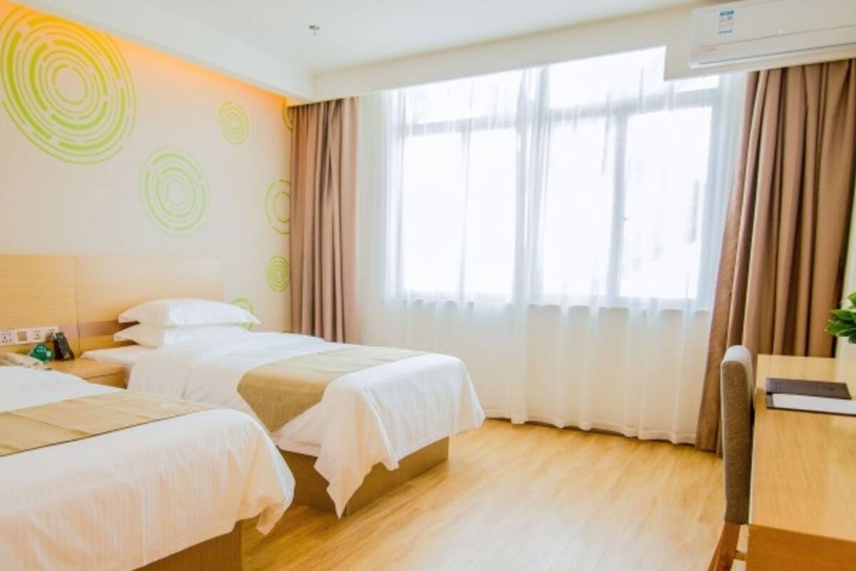 Habitación de hotel con dos camas, piso de madera, escritorio y ventana con cortinas.