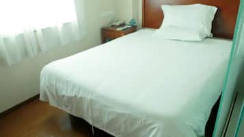 A hotel room with a large bed, a wooden headboard, a bedside table with a phone, and a window with curtains.