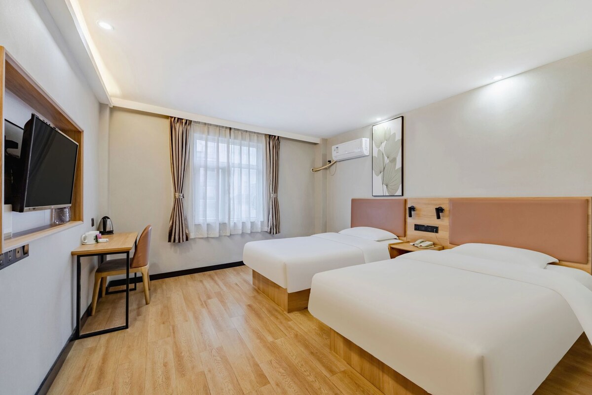 Una habitació d'hotel amb dos llits, un escriptori amb cadira, una televisió i una finestra amb cortines.