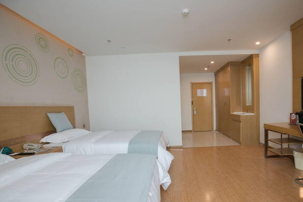 Una camera d'albergo con due letti, una scrivania e un bagno visibile attraverso una porta aperta.