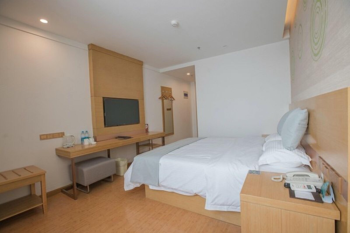 A hotel room with a bed, bedside table, desk, and a television.