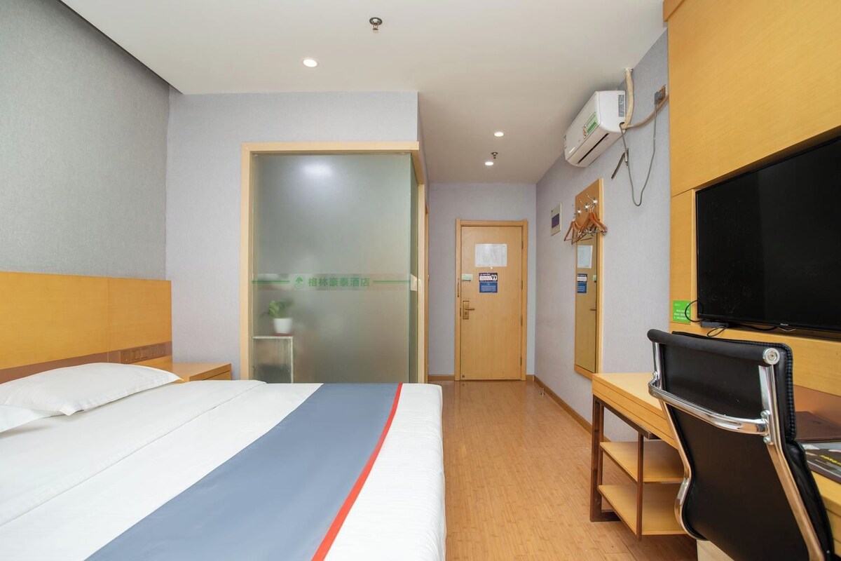 A hotel room with a bed, a desk, a television, and a door leading to a bathroom.