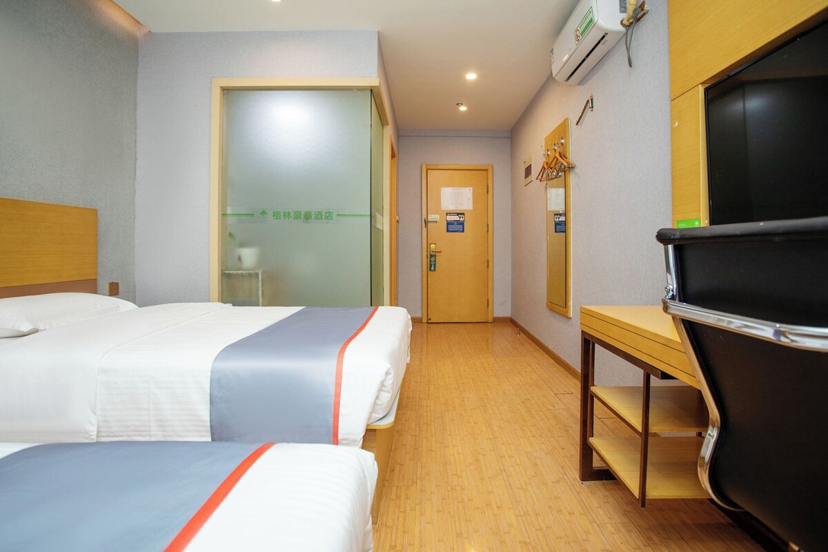 A hotel room with two beds, a desk, a chair, and a television.