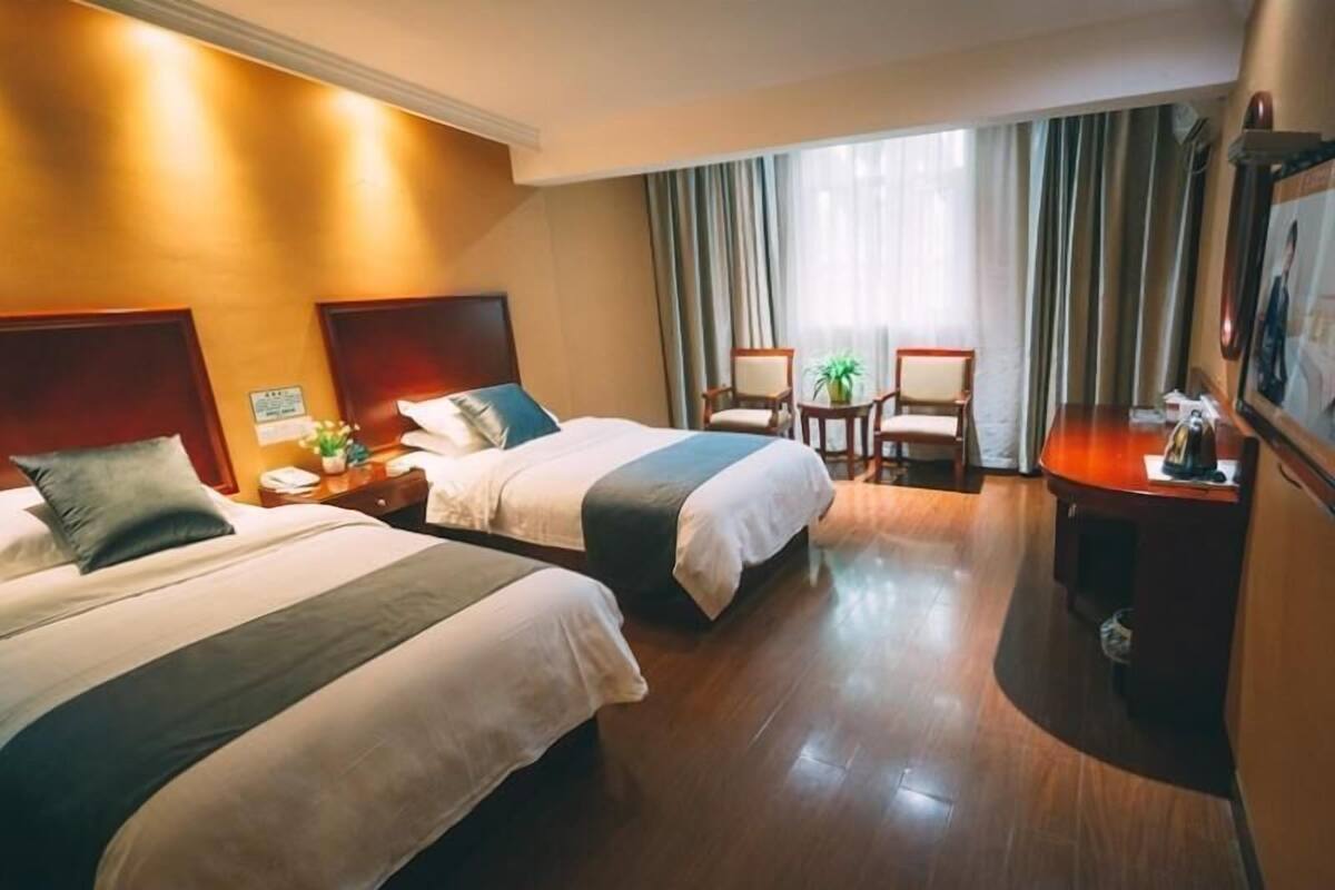 Une chambre d’hôtel avec deux lits, un bureau, une chaise et une fenêtre avec des rideaux.