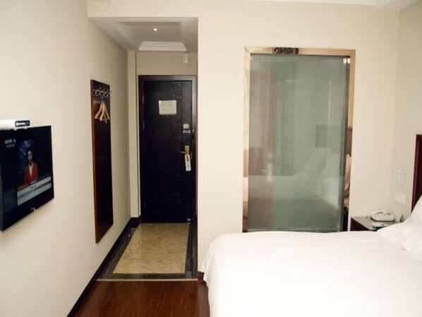 A hotel room with a bed, a television, a door, and a glass partition.