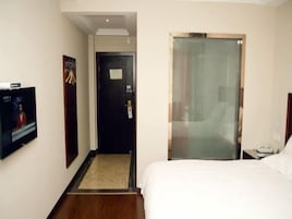 Una habitación de hotel con cama, televisión, puerta y separador de vidrio.
