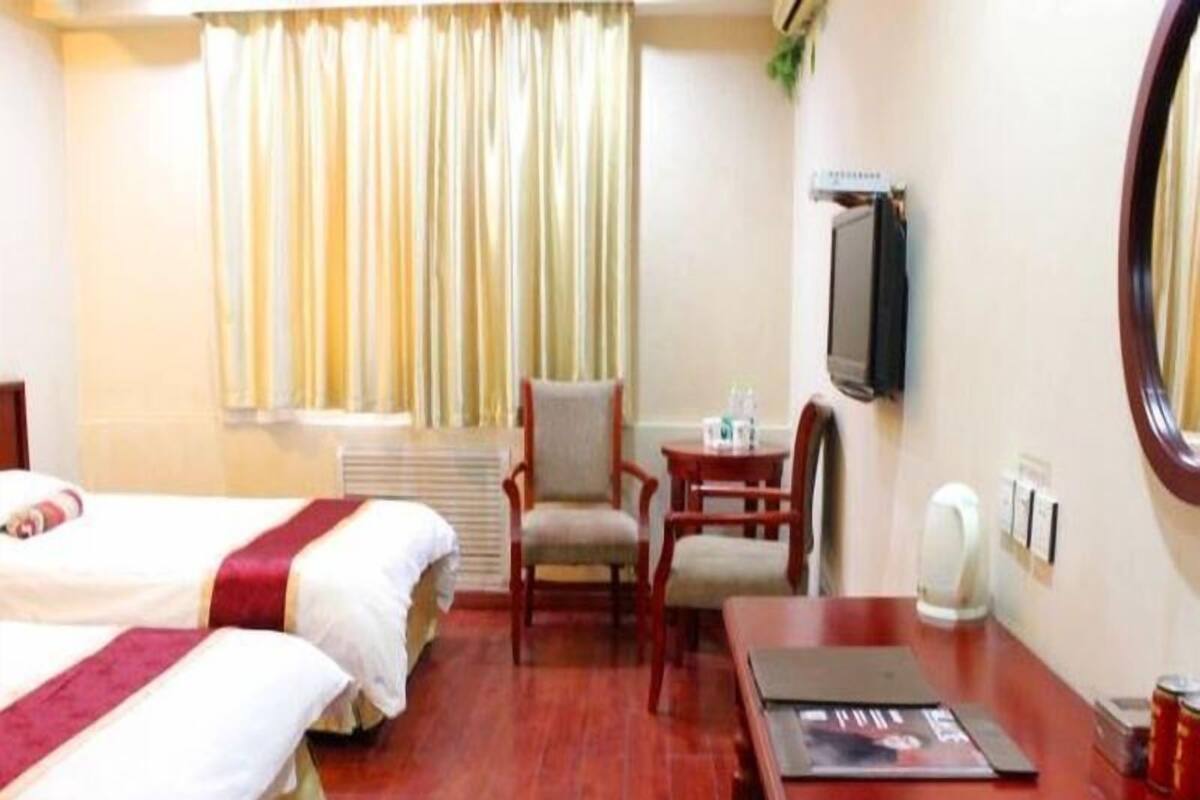 Une chambre d’hôtel avec deux lits, un bureau en bois, une chaise, une télévision et une fenêtre avec des rideaux.
