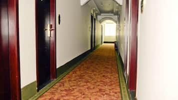 A hotel hallway with wooden doors, a patterned carpet, and a white wall.