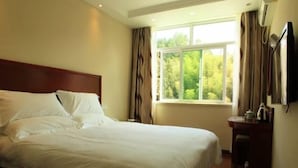 Habitación de hotel con cama, ventana con cortinas, mesita de noche y televisor montado en la pared.