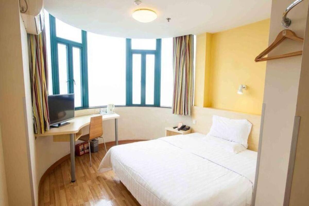 Ein Hotelzimmer mit Bett, Schreibtisch inklusive Computer, Stuhl, Fenster mit Vorhängen und einem Nachttisch.