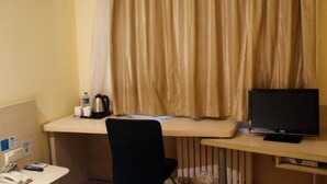 Quarto de hotel com escrivaninha, uma cadeira, televisão, cortina e uma mesinha de apoio com chaleira e chávena.