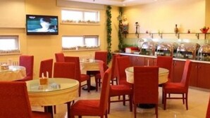 Restaurante com mesas redondas e cadeiras vermelhas, uma televisão na parede e um balcão de buffet com pratos expostos.