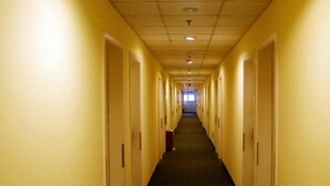 Corredor longo e estreito de um hotel, com portas em ambos os lados e piso coberto por carpete.