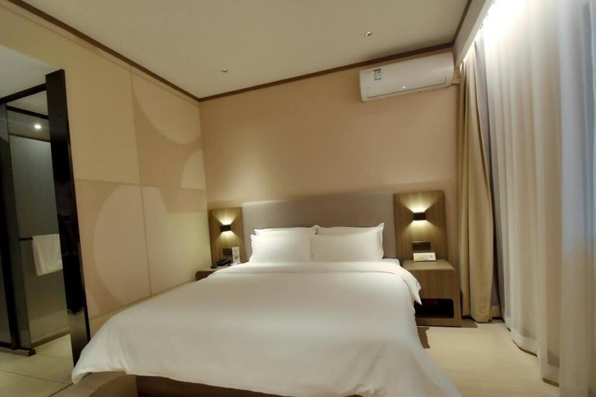 Et hotelværelse med en stor seng, sengeborde med lamper, et spejl og en aircondition.