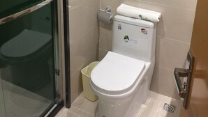 A bathroom with a toilet, a glass shower enclosure, and a trash bin. - Vatica Hotel (Xingtai)