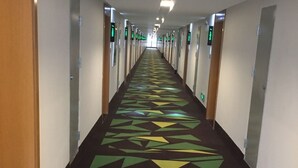 A long hallway with doors on both sides, each marked with a green sign. - Vatica Hotel (Xingtai)