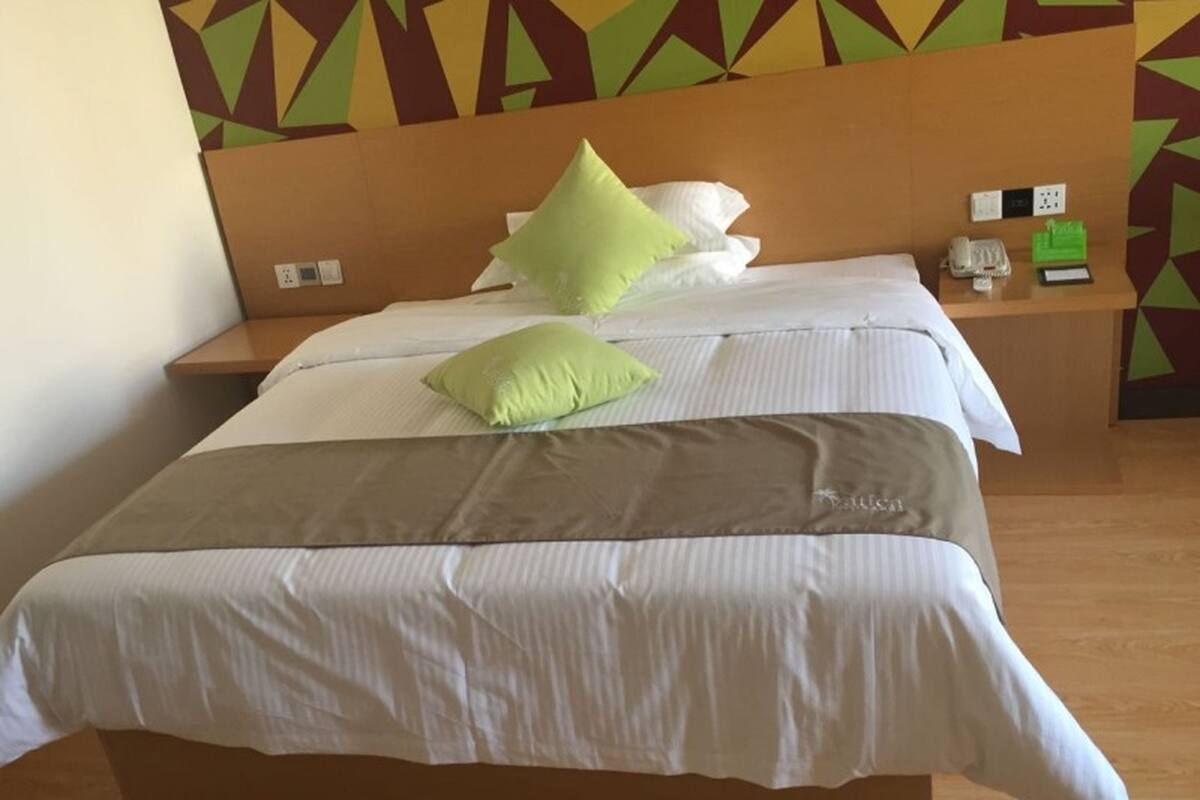 A hotel room with a bed, pillows, a nightstand, and a wall with geometric patterns.