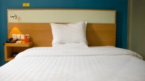 Una habitación de hotel con cama, mesita de noche, lámpara y teléfono instalado en la pared.