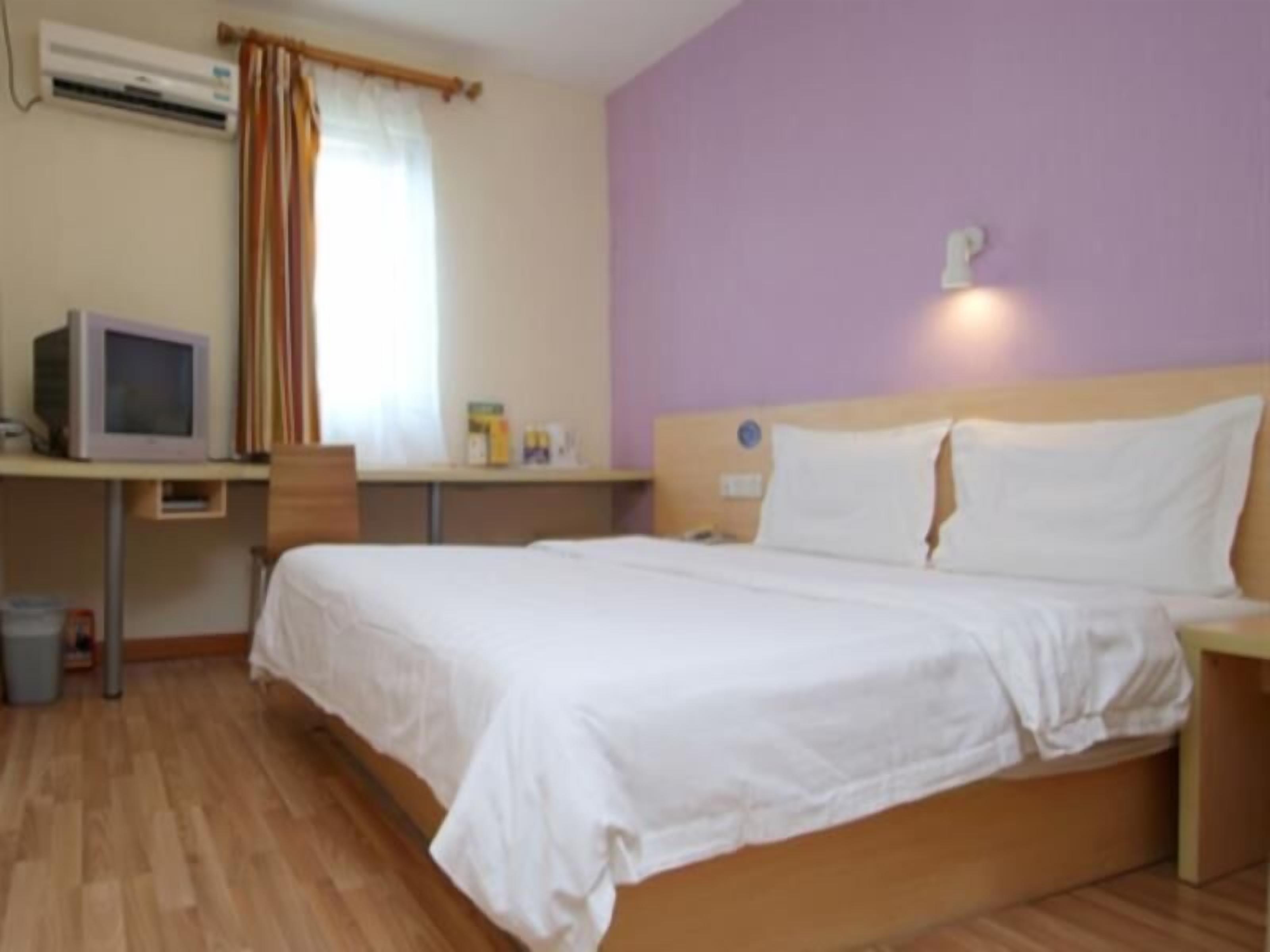 Une chambre à coucher comprenant un lit, un bureau avec un ordinateur, une fenêtre avec des rideaux et un appareil de climatisation.
