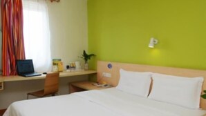 Habitación de hotel con cama, escritorio con una computadora portátil, una silla y una mesita con una planta.