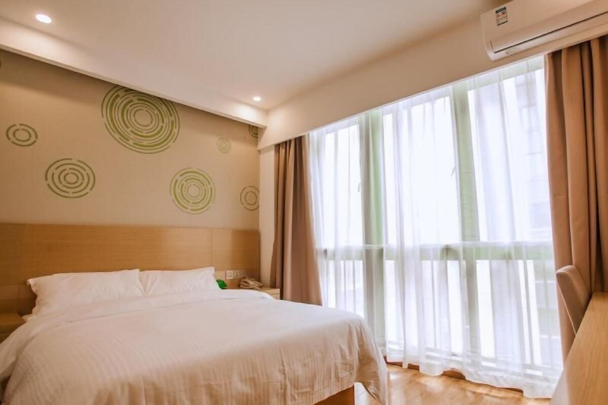 Habitación de hotel con cama, escritorio, silla, ventana con cortinas y unidad de aire acondicionado.
