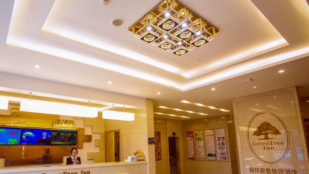 Uma área de recepção de hotel com um ecrã digital, um balcão de recepção e um logótipo na parede.