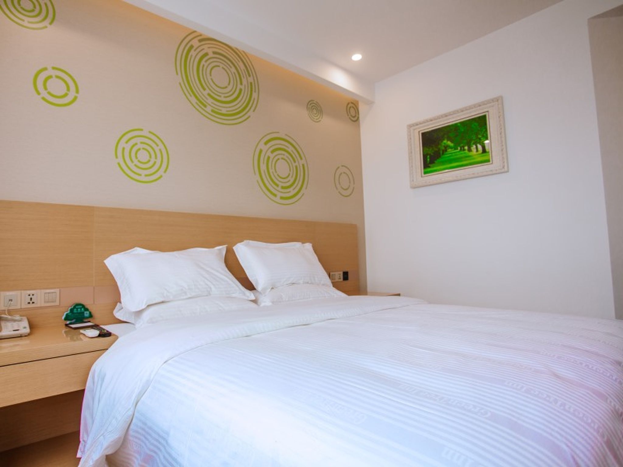 Una cama bien hecha con sábanas blancas, un cabecero de madera y una pared con diseños circulares verdes.