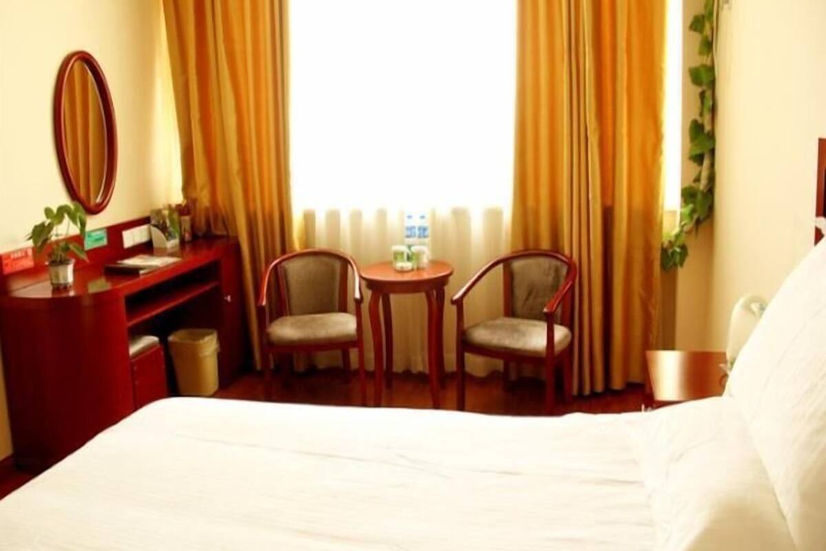 A hotel room with a bed, two chairs, a desk, and a mirror.