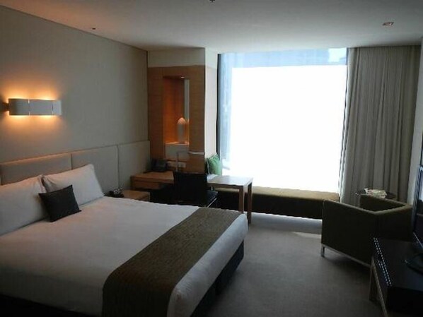 Una habitación de hotel con una cama grande, un escritorio, una silla y una ventana con cortinas.