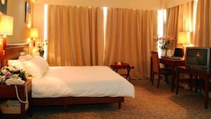 Une chambre d’hôtel avec un lit, un bureau, une chaise, une télévision et des rideaux.