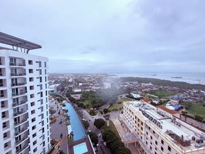 A high-rise building with a swimming pool, a view of the cityscape, and a body of water in the distance. - Mactan Newtown Beach Condo Unit 1-Bedroom - Starfish Sanctuary C417F (Lapu-Lapu)