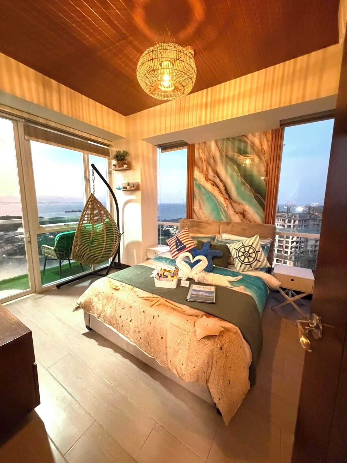 Un dormitorio con una cama grande, una silla colgante, vistas de la ciudad y un candelabro.
