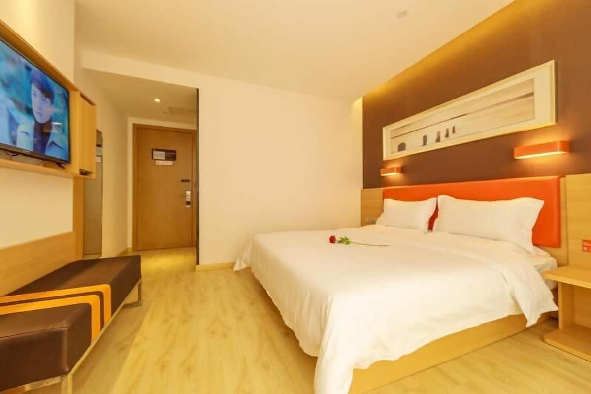 A hotel room with a bed, a TV, a bench, and a wooden floor.
