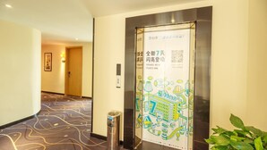 A hotel hallway with a patterned carpet, a trash bin, and a poster with a cityscape illustration. - 7 Days Premium Hotel (Chengdu)