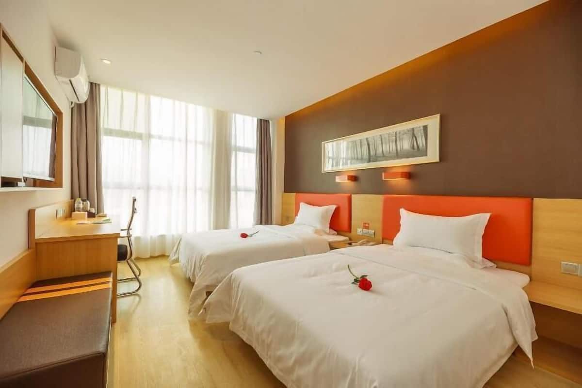 A hotel room with two beds, a desk, a chair, and a large window.