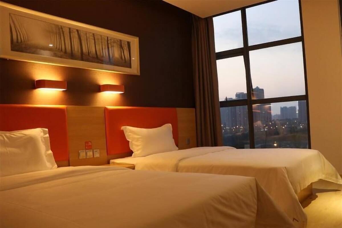 A hotel room with two beds, a city view, and a painting on the wall.
