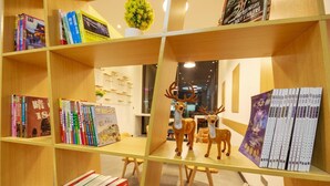 A library with bookshelves, a decorative deer sculpture, and a wall with a floral arrangement. - 7 Days Premium Hotel (Chengdu)