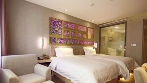 Une chambre d’hôtel avec un grand lit, deux fauteuils, une table de chevet avec une lampe et une cabine de douche en verre.