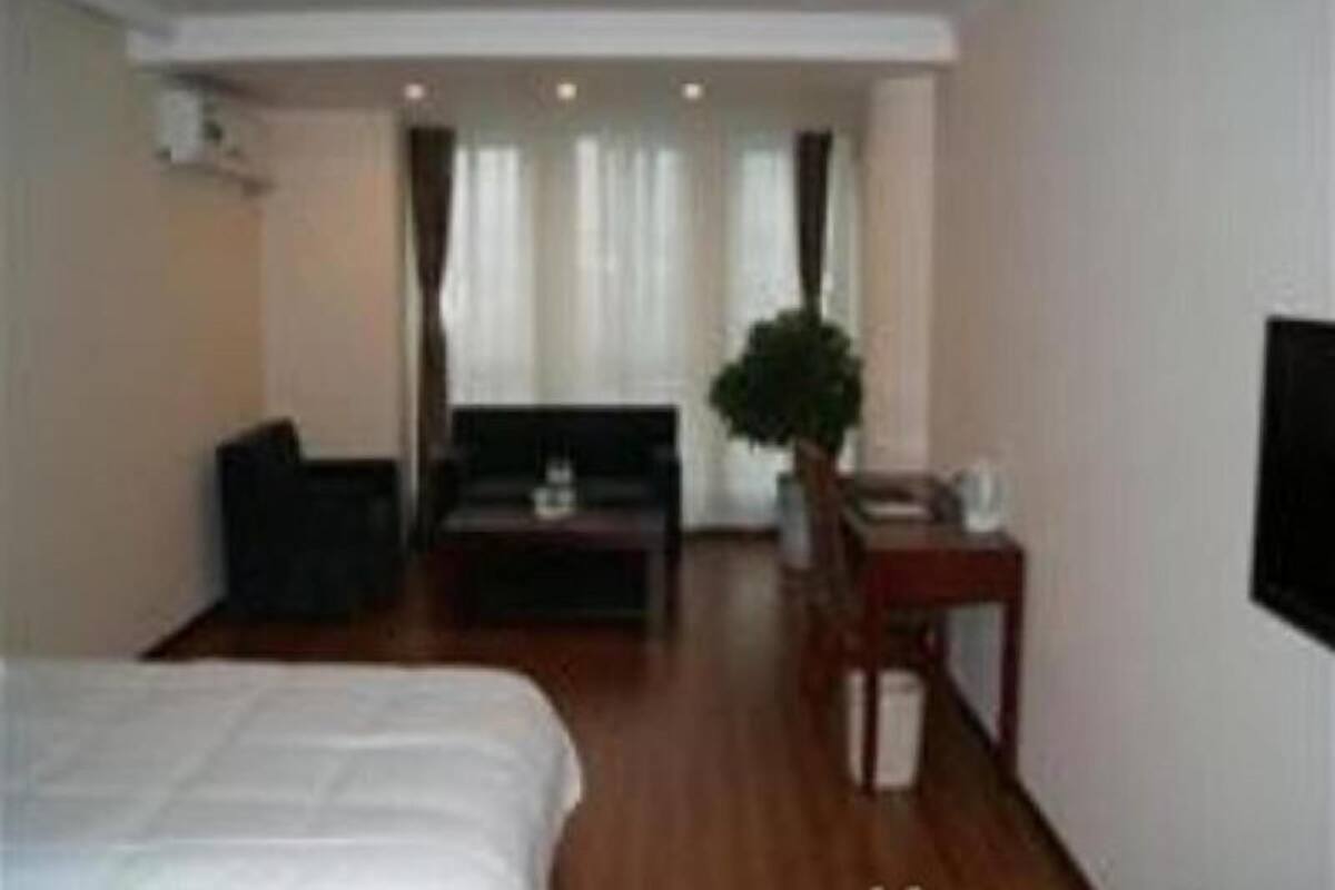 A hotel room with a bed, a desk, a chair, a small table, a potted plant, and a television.