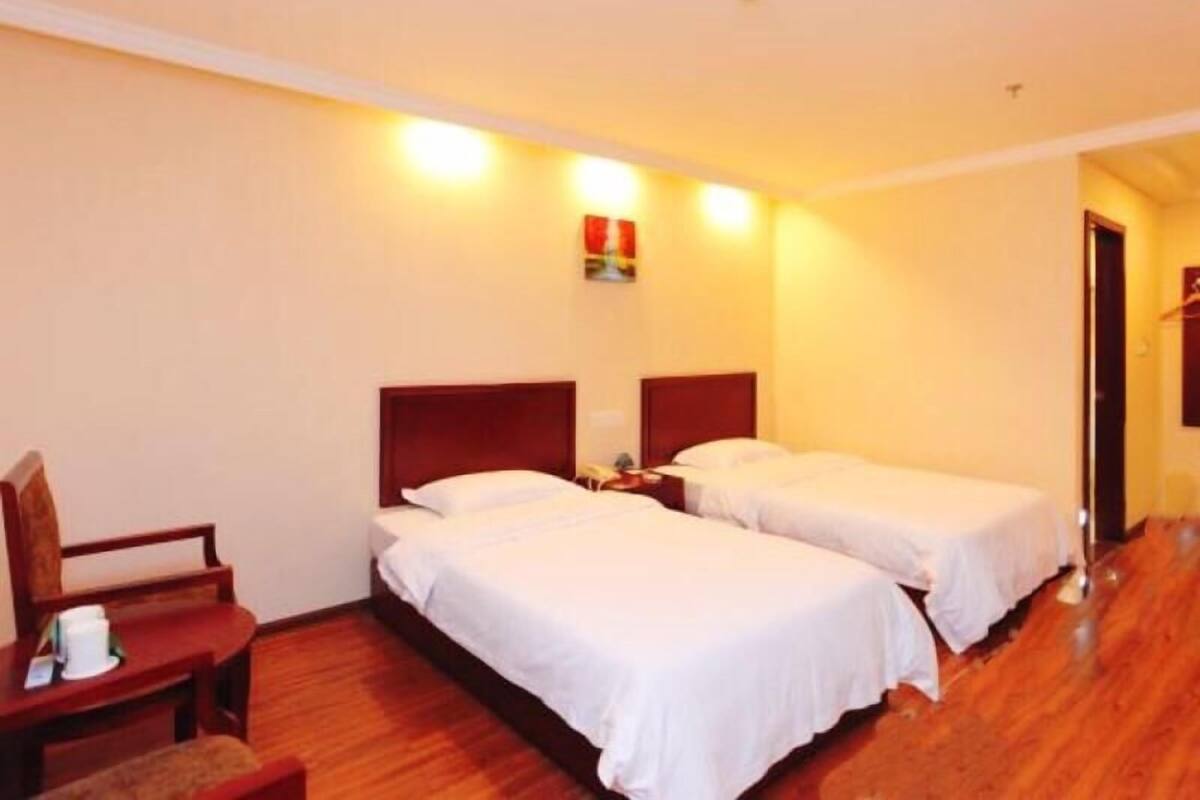 A hotel room with two single beds, a wooden chair, a small table, and a nightstand.